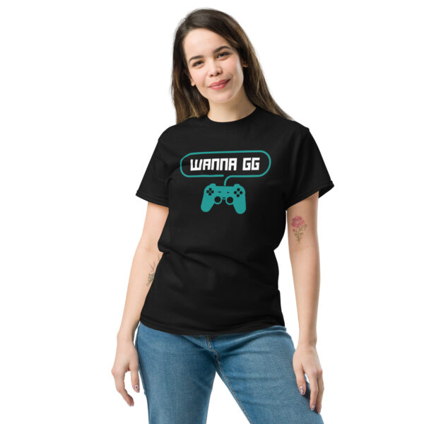 A woman posing head-on wearing a black tshirt on which is written "wanna gg" in white with a green PlayStation controller underneath