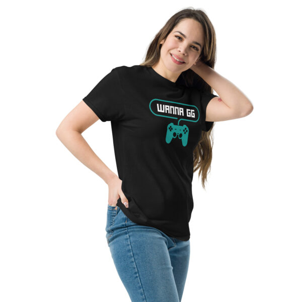 A woman posing head-on wearing a black tshirt on which is written "wanna gg" in white with a green PlayStation controller underneath