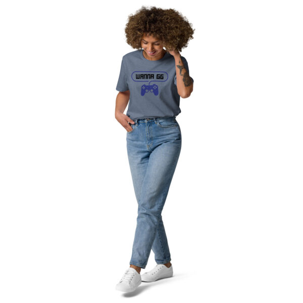 A woman posing head-on wearing a grey tshirt on which is writting "wanna gg" in black with a blue PlayStation controller