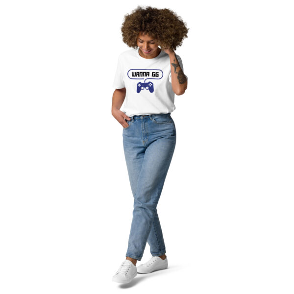 A woman posing head-on wearing a white tshirt on which is writting "wanna gg" in black with a blue PlayStation controller