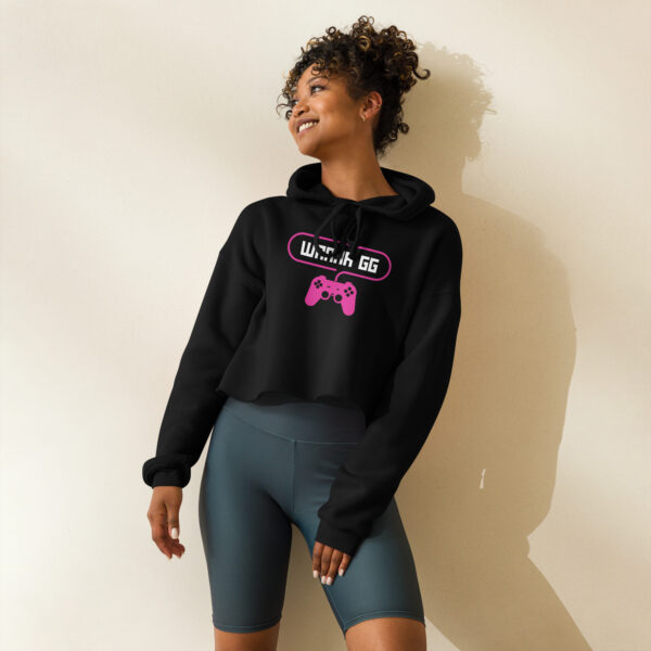 A woman posing head-on wearing a black sweatshirt on which is writting "wanna gg" in white with a pink PlayStation controller