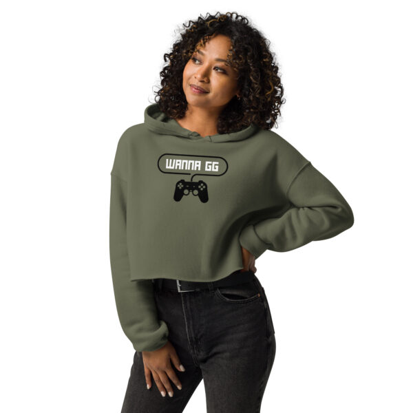 A woman posing head-on wearing a khaki-coloured sweatshirt on which is writting "wanna gg" in white with a black PlayStation controller underneath