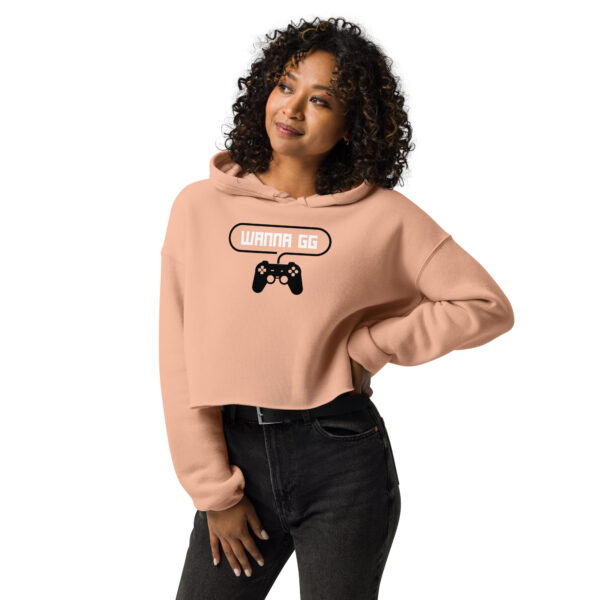 A woman posing head-on wearing a sweatshirt on which is writting "wanna gg" in white with a black PlayStation controller underneath